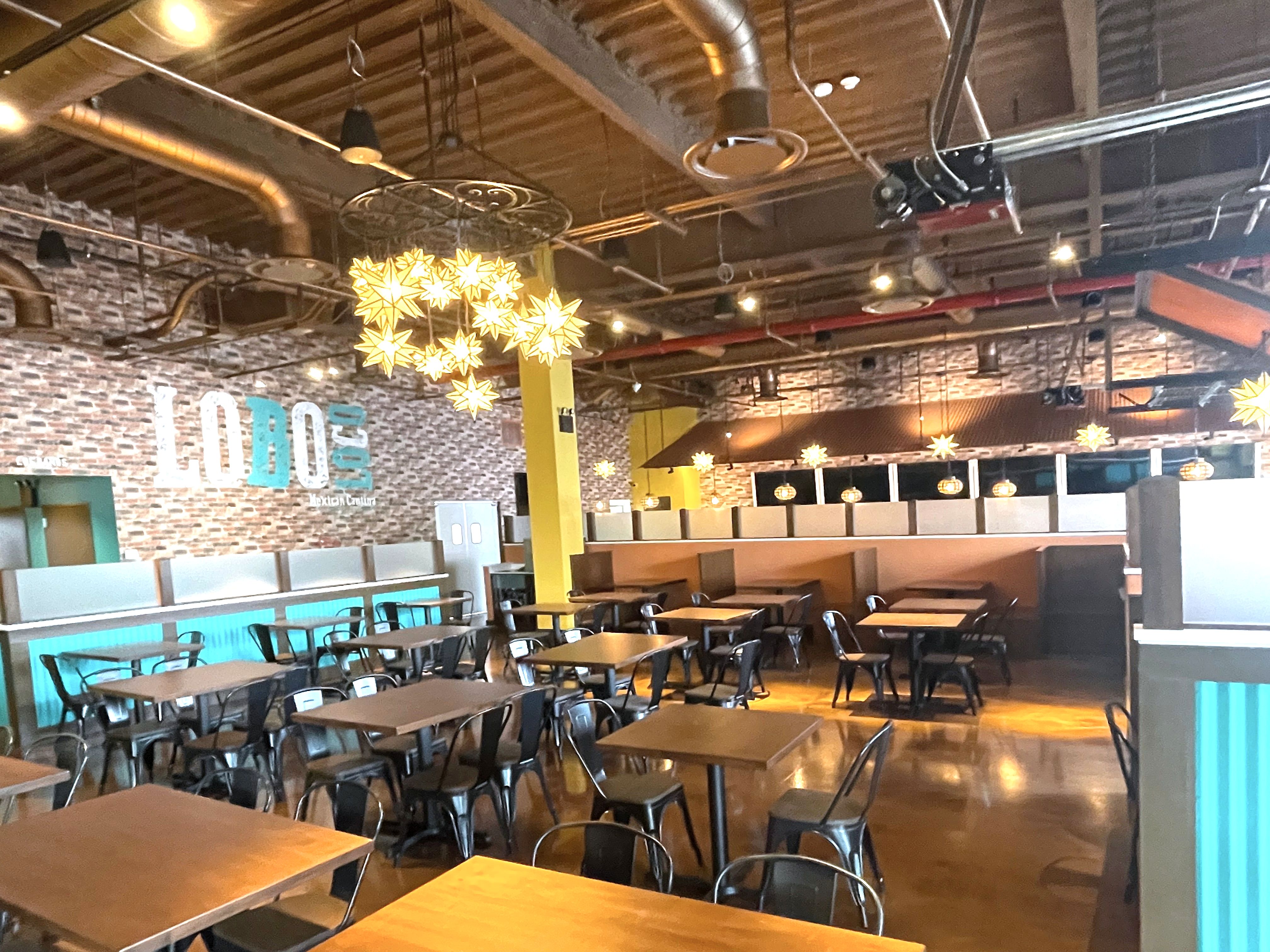 Wide restaurant dining room with tables, star chandeliers and exposed ceiling